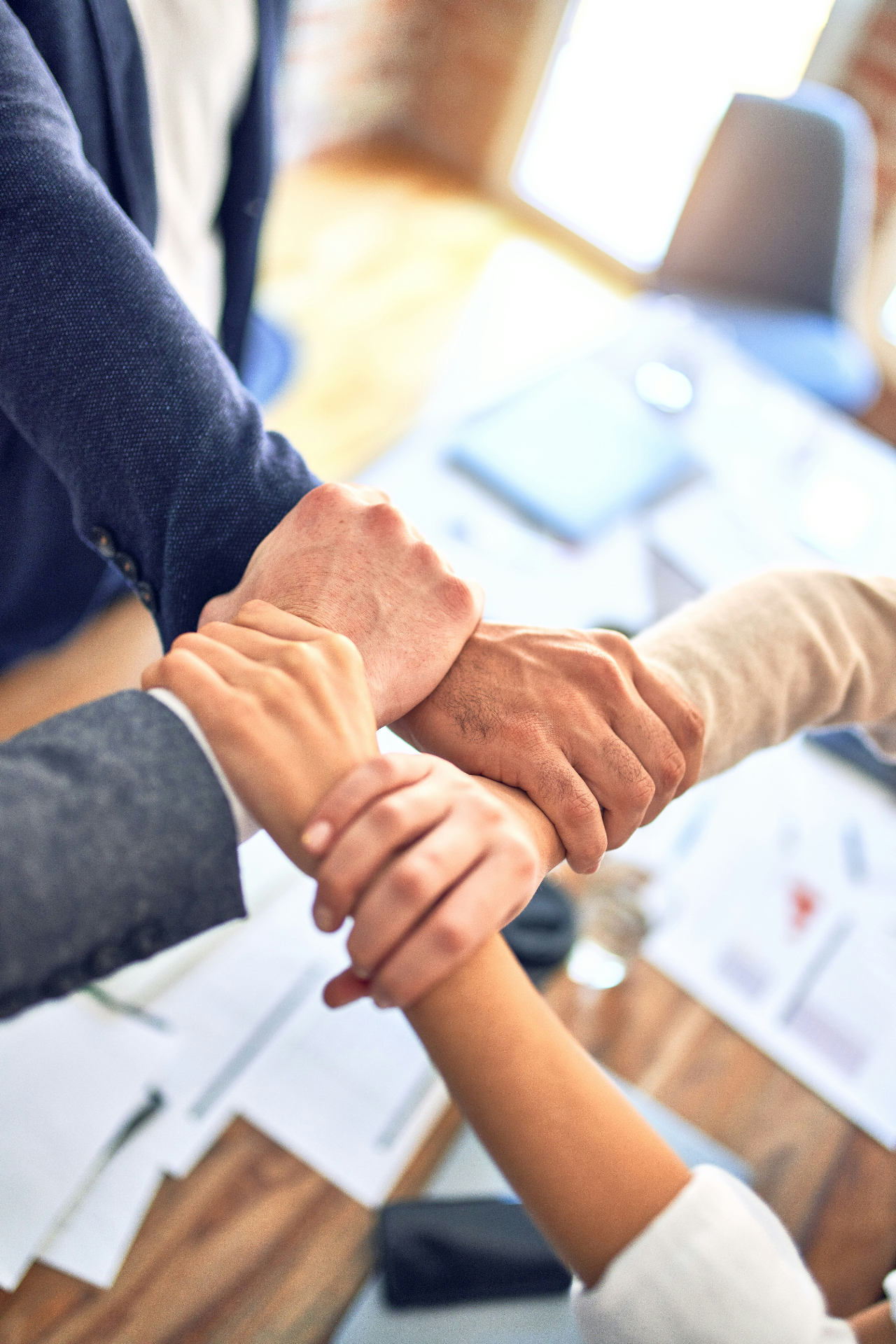 Colleagues joining hands together over a workplace meeting table.